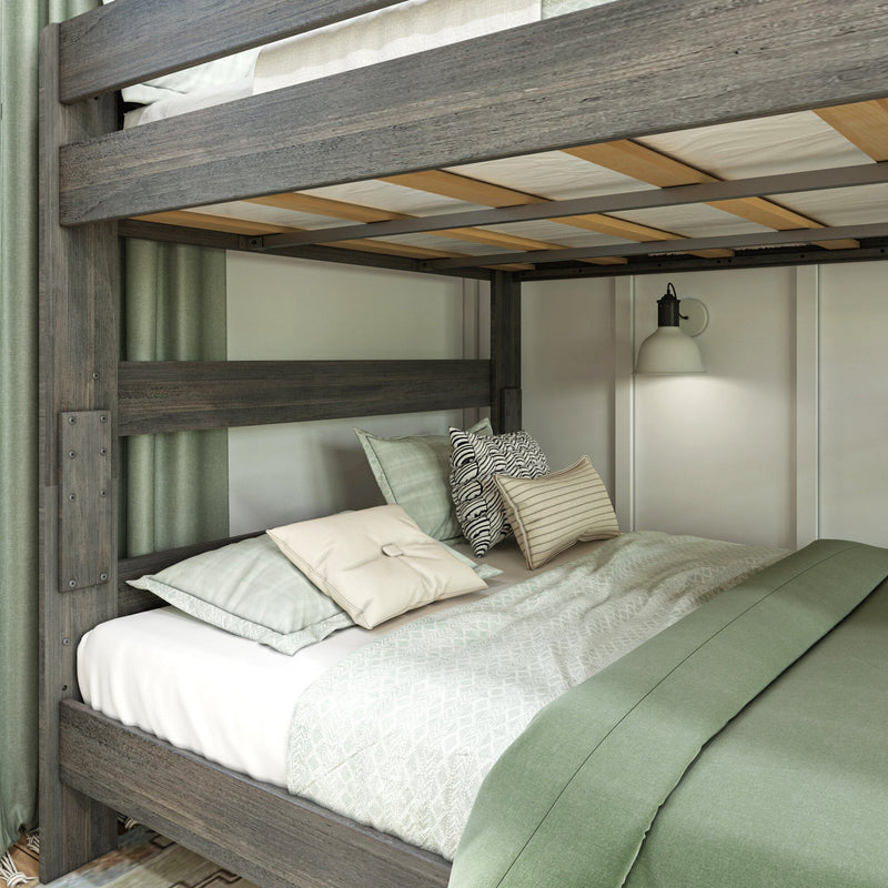 Gray rustic wooden bunk bed with sage green bedding, patterned throw pillows, visible slatted bed base and wall-mounted bedside lamp in cozy bedroom