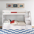 White wooden loft bunk bed with staircase, car-themed sheets and pillows, framed vintage car prints on wall and blue checkered rug in children's bedroom