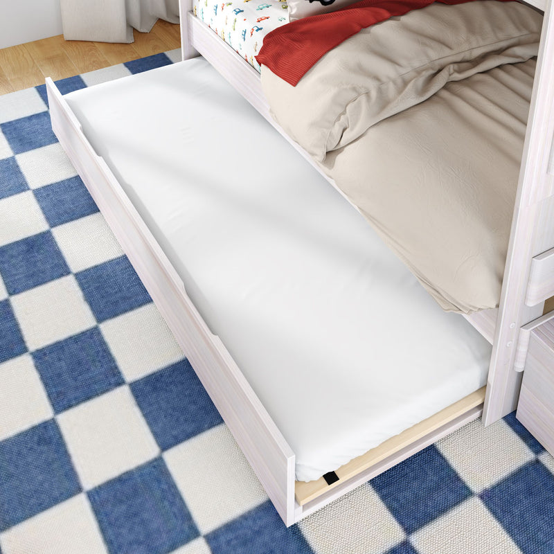 Pull-out trundle bed with white mattress under a white wood children's bed featuring car-print sheets and a blue checkered rug