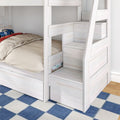 White wooden bunk bed with built-in storage stairs and drawers, beige bedding and car-themed pillow on lower bunk in a kids' room with blue checkered rug