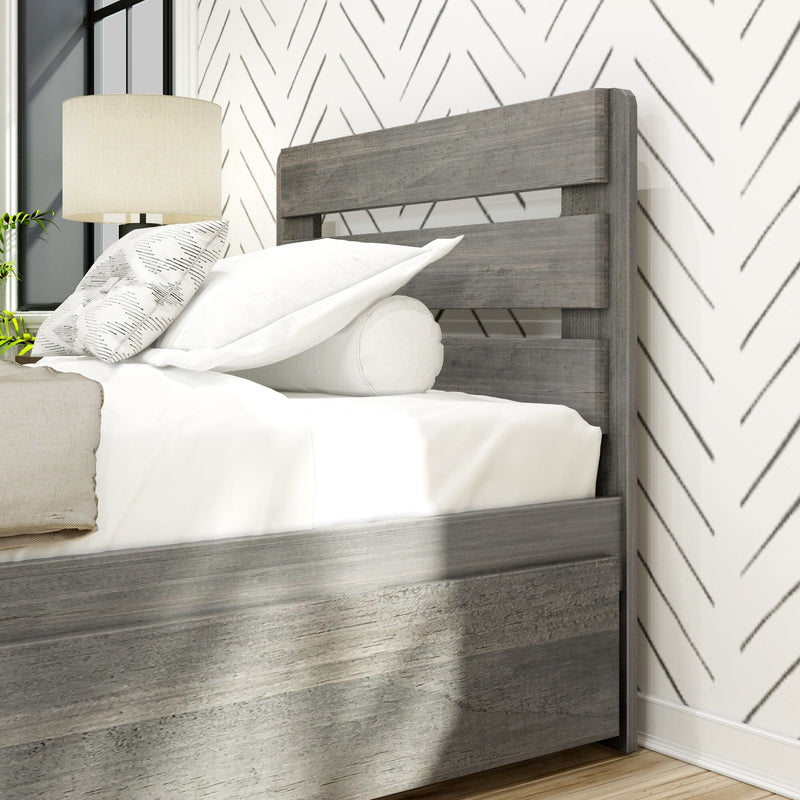 Close-up of modern rustic gray wood bed with slatted headboard, white linens, patterned chevron wallpaper and bedside lamp