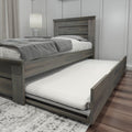 Gray wooden platform bed with pull-out trundle mattress, gray bedding and bedside lamp in a modern bedroom