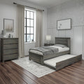 Modern farmhouse bedroom with gray wood twin bed and pull-out trundle, matching dresser and nightstand, beige curtains, patterned rug and dark hardwood floors