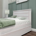 Cozy modern bedroom with sage green board-and-batten accent wall, whitewashed wood bed frame, green linens and bedside lamp
