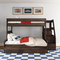 Dark walnut kids bunk bed with built-in staircase storage, car-print bedding and pillow, red throw blanket, blue check rug, and three framed vintage car posters on a white wall