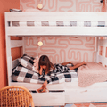 Cozy pink kids bunk bed with checkered bedding, knit blanket, under-bed drawer and child reading a book