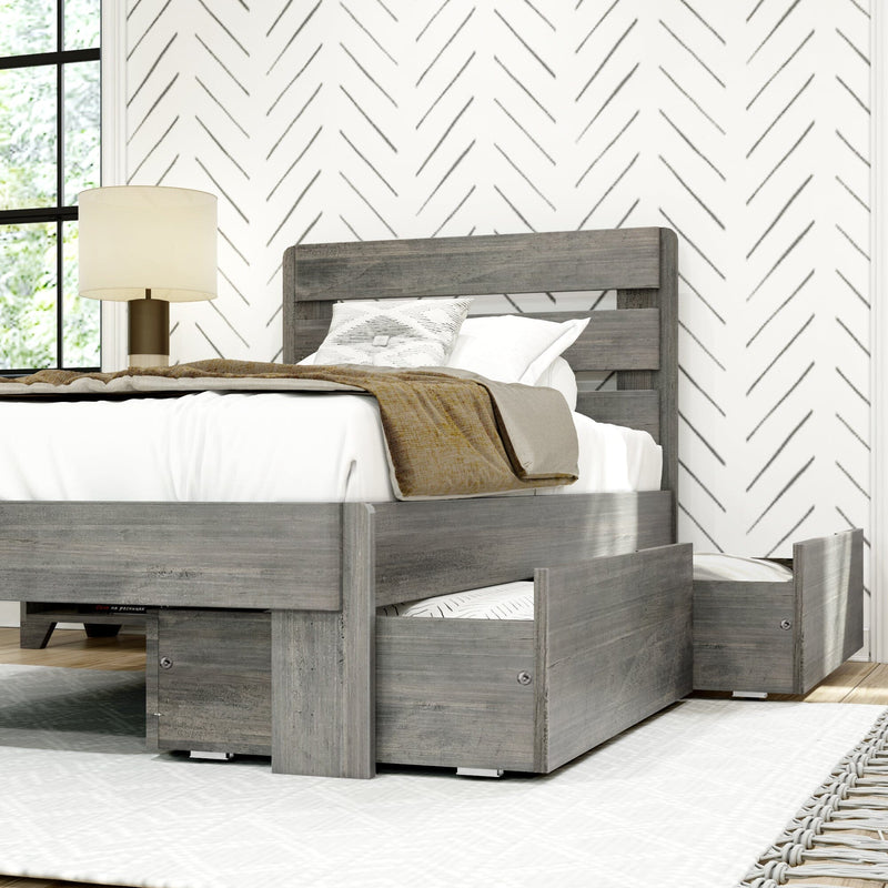 Gray wood platform bed with under-bed trundle and storage drawers, white bedding and beige throw, bedside lamp and chevron wallpaper in a modern farmhouse bedroom with natural light