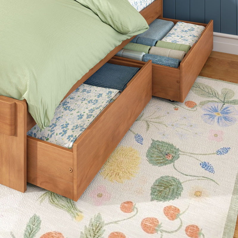 Under-bed wooden storage drawers filled with neatly folded linens, green duvet and blue bedding in an organized bedroom with floral rug