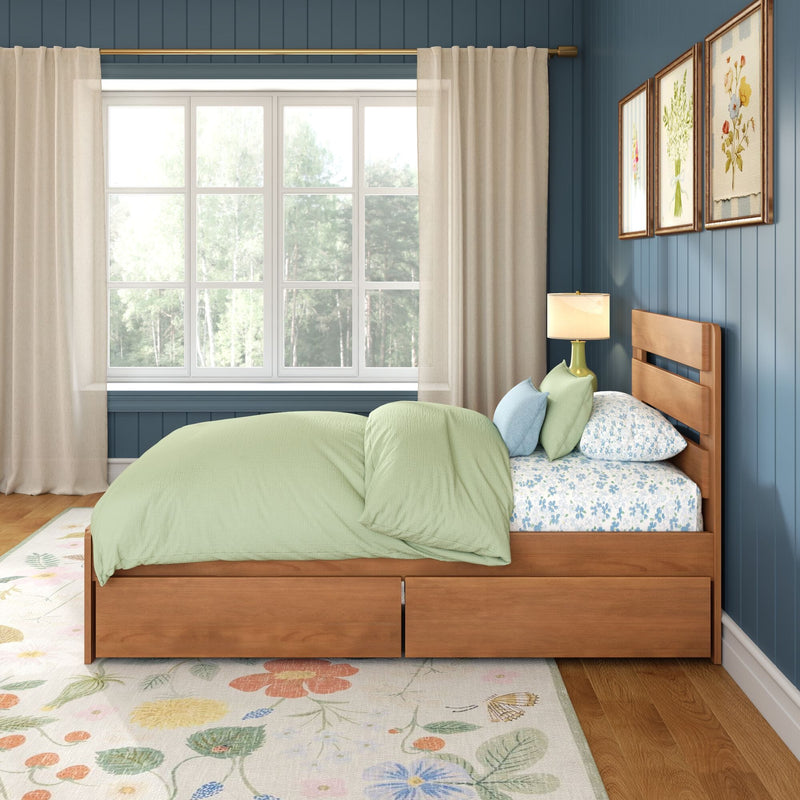 Cozy modern bedroom with light green bedding on a wooden platform bed with drawers, floral area rug, blue paneled accent wall, large window with sheer beige curtains, bedside lamp and botanical wall art