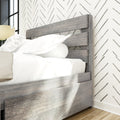 Gray wooden slatted bed frame with white bedding, chevron wallpaper, bedside lamp and hardwood floor in modern farmhouse bedroom