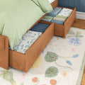 Under-bed wooden storage drawers with neatly folded quilts and linens beneath a green-bedspread platform bed on a floral rug
