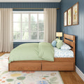 Cozy bedroom with wooden platform bed, light green bedding and floral sheets, floral area rug, blue vertical-paneled accent wall with framed botanical prints, large window with sheer curtains and brass curtain rod
