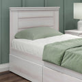 Whitewashed wooden platform twin bed with built-in underbed storage drawers, sage green bedding, matching nightstand and lamp in modern bedroom