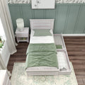 Whitewashed twin bed with pull-out trundle and sage green bedding against a board-and-batten accent wall, white nightstand with lamp, sheer curtains and hardwood floors