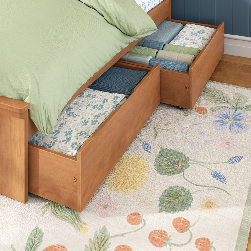 Under-bed storage drawers in wooden bed frame with folded linens, light green bedding and floral rug — bedroom storage solution