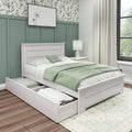 Whitewashed wooden storage bed with open under-bed drawers, green bedding and pillows against a sage green paneled accent wall topped with botanical wallpaper, white nightstand with lamp, neutral curtains and hardwood floors in a modern farmhouse bedroom