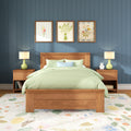 Modern farmhouse bedroom with wooden bed frame and green bedding, blue paneled wall with three framed floral prints, matching green bedside lamps, wooden nightstands and floral rug