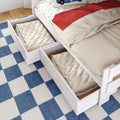Under-bed storage drawers filled with folded quilts and blankets beneath a white wooden kids bed with car-print fitted sheet, red throw, and blue checkered rug