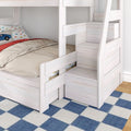 Whitewashed wooden bunk bed with built-in storage stairs, beige bedding and car-print pillow in a kids' bedroom on blue checkered rug