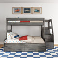 Gray wooden bunk bed with stairs and built-in drawers, car-print bedding, blue checkered rug and framed vintage car posters above