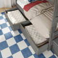 Grey wooden bunk bed with pull-out under-bed storage drawers, beige bedding, car-print sheet and blue checkered rug in a children's bedroom