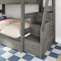 Gray wood twin-over-twin bunk bed with built-in storage stairs and ladder, beige bedding, blue race car pillow and checkered blue rug in kids' bedroom