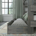Gray wooden bunk bed with pull-out trundle, green bedding and patterned pillow by window with sheer curtains in a cozy bedroom