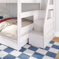 Whitewashed wooden bunk bed with built-in storage stairs, lower bed with beige bedding and car-print pillow on blue checkered rug — space-saving kids bedroom furniture