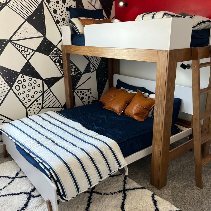 Modern wooden bunk bed with navy bedding, striped white-and-blue comforter, tan leather pillows and black-and-white geometric accent wall in kids' bedroom