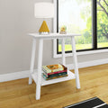 White wooden accent side table with lower shelf stacked books, yellow cone table lamp and glass orb by window in a bright modern living room with hardwood floors