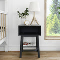 Scandinavian bedroom nightstand with black bedside table, wooden tripod lamp with white shade, white ribbed vase with greenery and gold-accent clock by window with forest view