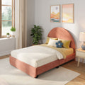 Sunlit modern bedroom with coral upholstered bed, neutral quilted bedding, decorative pillows including a blue flower cushion, potted plants, and pastel framed landscape wall art
