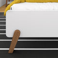 Close-up of modern white platform bed footboard with wooden legs, yellow quilt and black-and-white striped rug for contemporary bedroom decor