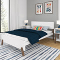 Modern Scandinavian bedroom interior with white platform bed, navy quilt, colorful striped pillow, blue bedside lamps, abstract framed art and striped area rug