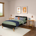 Children's bedroom with green bedding and navy striped pillows, plush toy on a black platform bed, wooden nightstands with copper lamps, framed animal prints on wall, light area rug and hardwood floor, modern kids room decor