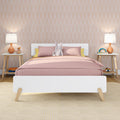 Modern kids' bedroom with pink bedding and stuffed bunny on a white bed, pastel arch-pattern wallpaper, wooden nightstands, orange bedside lamps and playful toys — nursery decor inspiration.