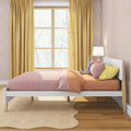 Kids' bedroom with pink and yellow bedding, stuffed bunny on bed, mustard curtains, patterned wallpaper, wooden window and bedside lamp