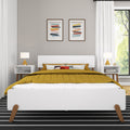 Contemporary modern bedroom with white mid-century bed frame, mustard yellow quilt and decorative pillows, matching white nightstands with gold table lamps, abstract framed wall art on a neutral gray wall, white curtains and sunlit window