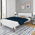 Modern minimalist bedroom with white bed, navy quilt, rainbow pillow, abstract framed art, bedside lamp and striped area rug