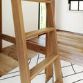 Natural oak ladder shelf with slatted steps in a bright modern room on hardwood floor over a black-and-white geometric rug