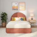 Modern bedroom decor with terracotta rounded upholstered headboard, beige striped bedding, yellow accent pillows and blue flower cushion, wooden nightstand with ceramic lamp, framed pastel abstract art, and potted fiddle leaf fig plant.