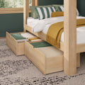 Solid wood four-poster bed with under-bed storage drawers, white linen, green striped pillows and mustard throw in a cozy modern bedroom