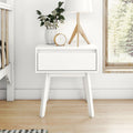 White mid-century modern bedside table (nightstand) with single drawer, wooden tripod lamp, white ceramic vase with blossoms and small gold clock by window on light wood floor — minimalist Scandinavian bedroom decor