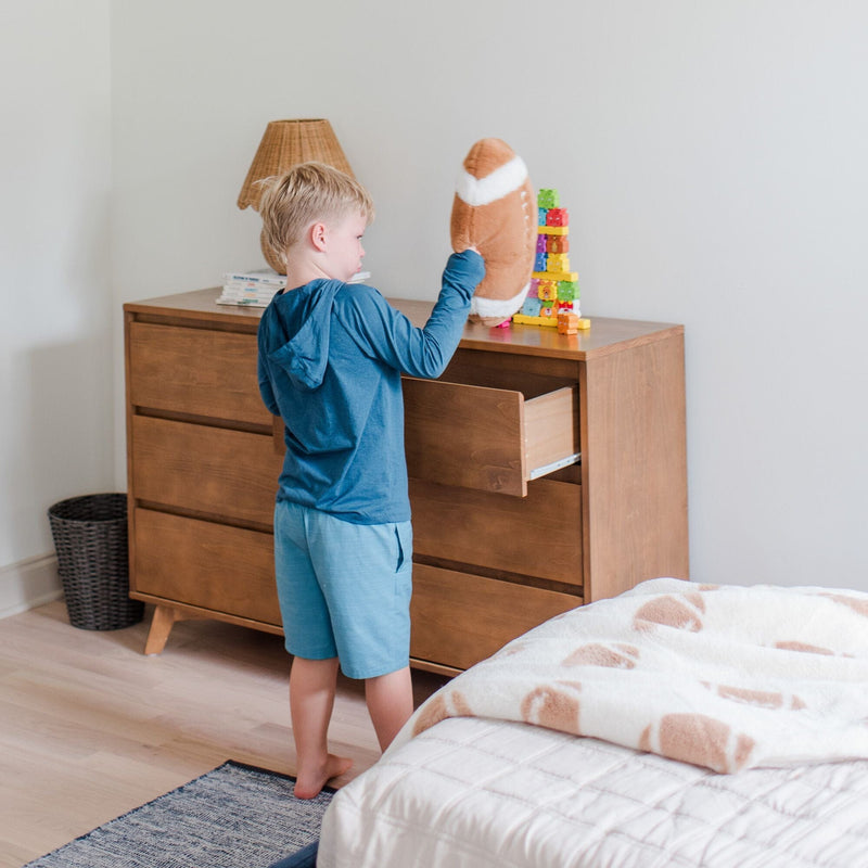 Child organizing toys on a wooden dresser in a bright modern bedroom with a plush football and colorful stacking blocks.