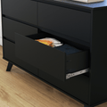 Matte black dresser with an open drawer revealing folded clothes on a hardwood floor — modern bedroom storage with metal drawer slides