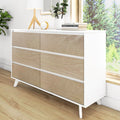 Minimalist mid-century modern white dresser with six natural wood drawers and tapered legs, styled with lamp, plant and books in bright bedroom