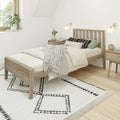 Minimalist Scandinavian bedroom with light wood bed frame, neutral bedding and layered throw, patterned rug, bedside tables, wall sconces, and potted plant