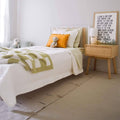 Cozy neutral kids bedroom with white toddler bed, green check bedding, orange pom-pom pillow, stuffed animals, wooden nightstand, lamp and framed typographic wall art