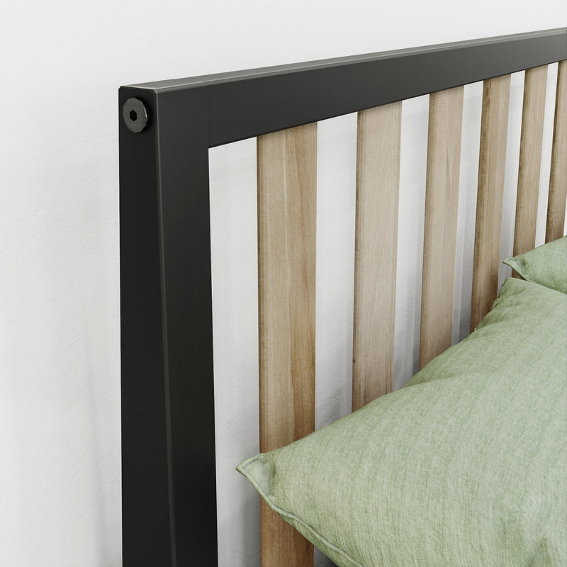 Close-up of modern bed headboard with black metal frame and light oak vertical slats next to green linen pillow on a white wall, minimalist bedroom decor