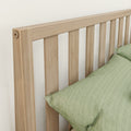 Light oak slatted headboard close-up with vertical slats and green linen pillow on minimalist bed